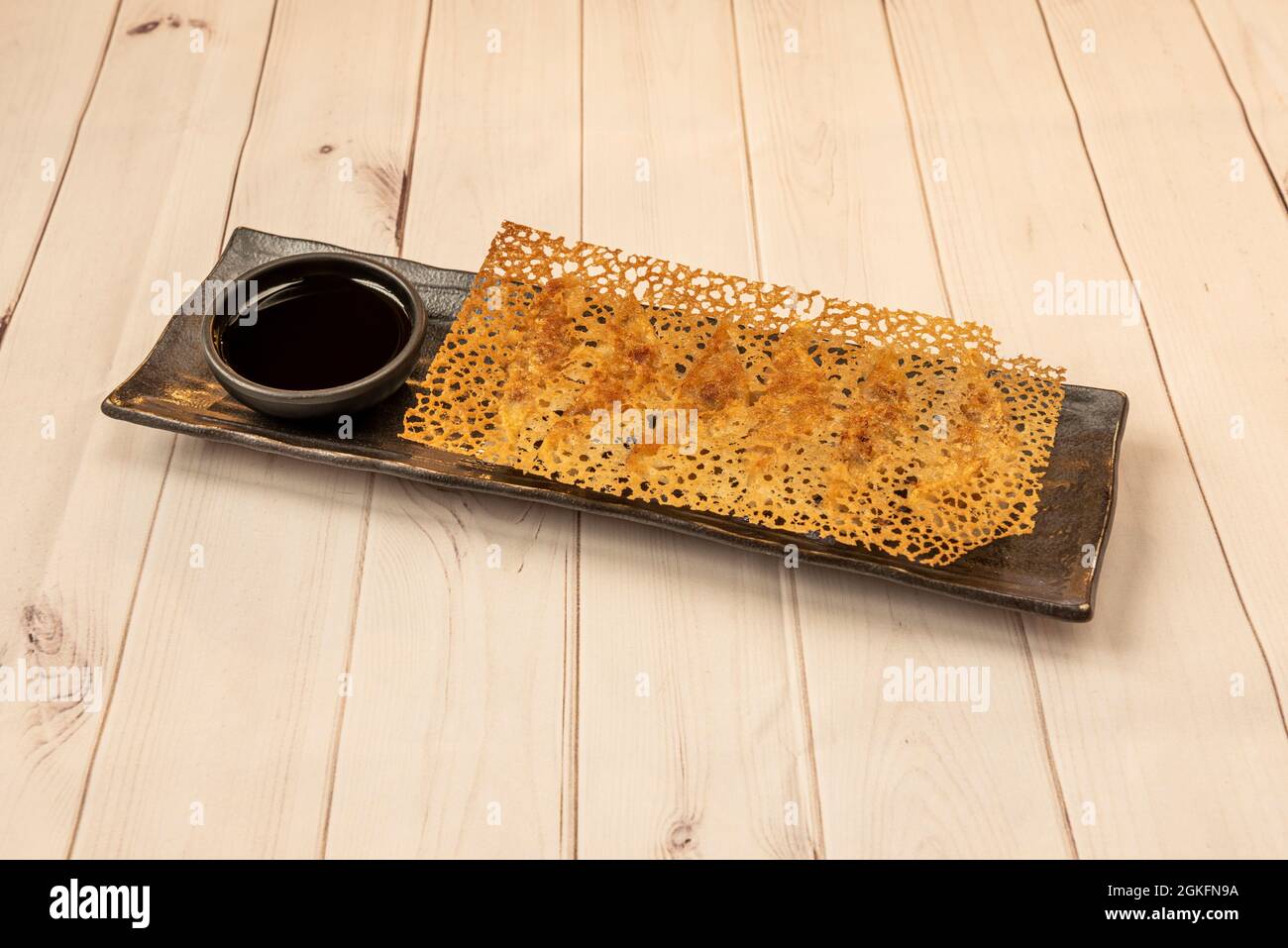 Gnocchi giapponesi, gyozas, conditi con formaggio croccante su piatto nero con piccolo contenitore di salsa di soia Foto Stock