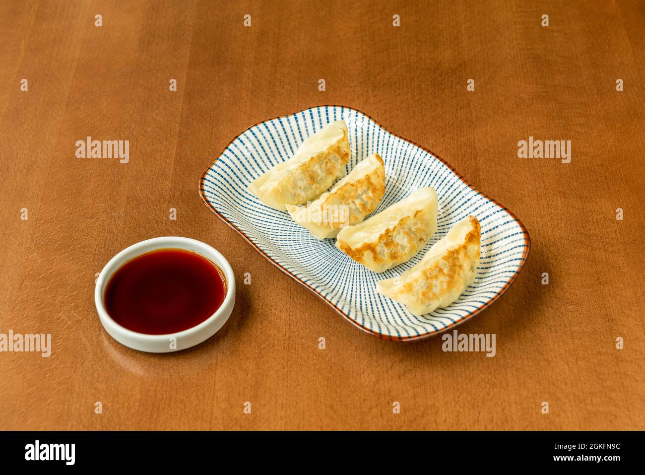 Gnocchi cinesi farciti di verdure cotte sul grill su un piatto decorato con linee blu e un piccolo contenitore con salsa di soia Foto Stock
