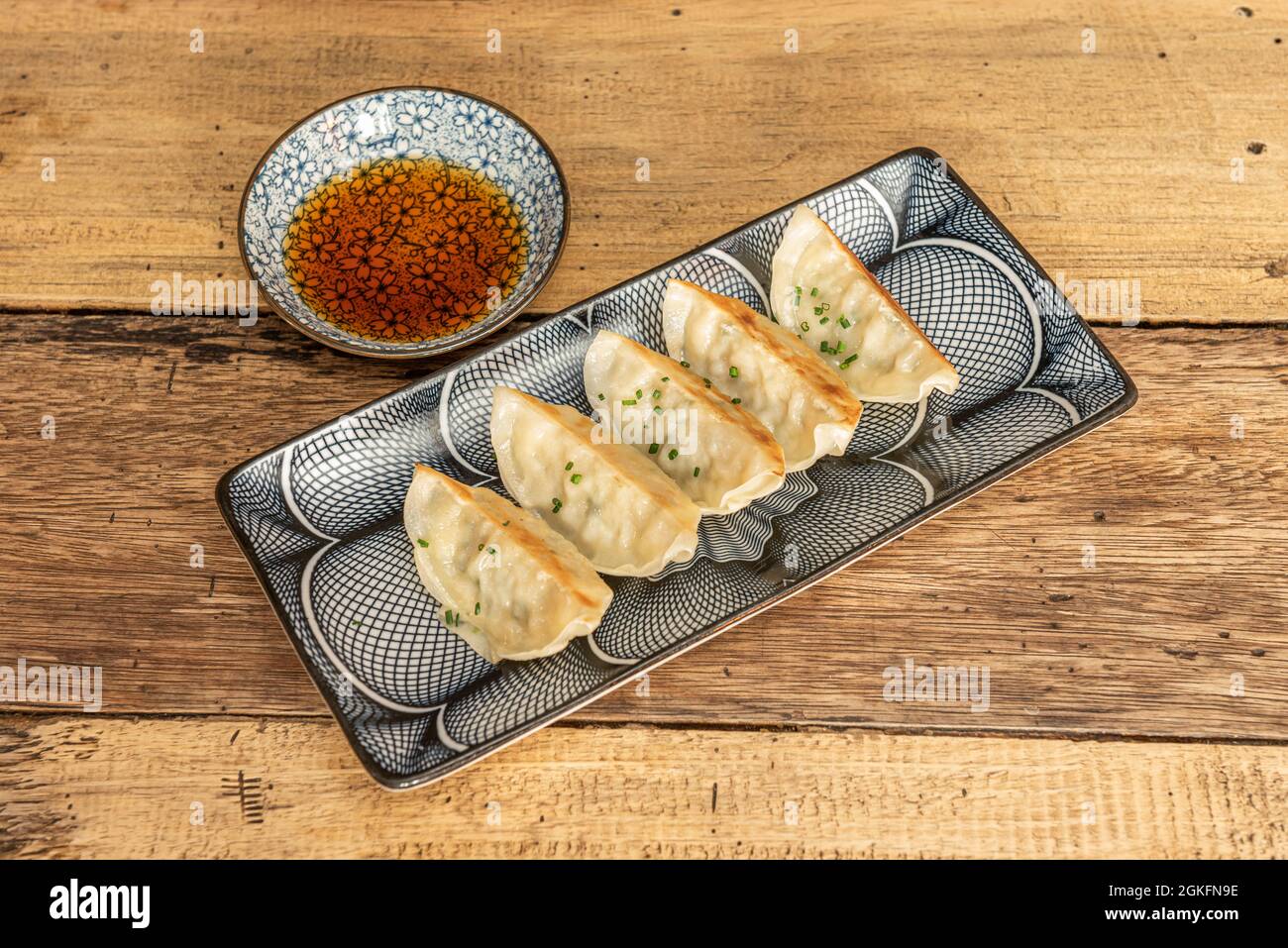 porzione di gyozas fritto sul grill, dim sum, con salsa di soia, erba cipollina tritata su piatti decorati Foto Stock