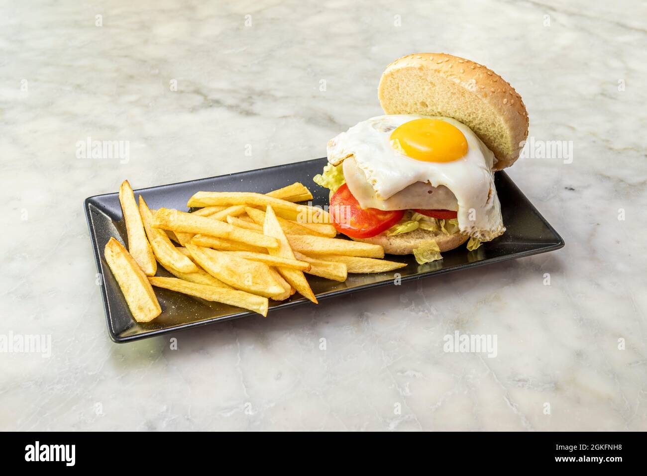 Hamburger di manzo classico con formaggio e uova fritte con guarnitura di patate su un tavolo di marmo bianco Foto Stock