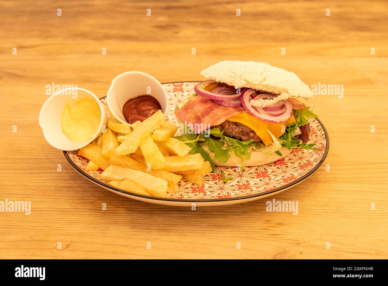 Cheeseburger, pancetta, cipolla rossa, patatine fritte fatte in casa, rucola, formaggio cheddar, ketchup e maionese su un piatto colorato Foto Stock