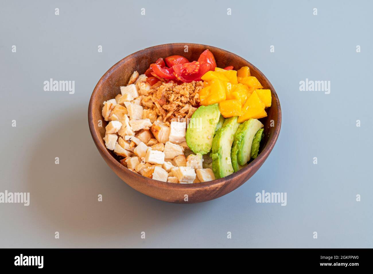 Una sana ciotola di pollo e verdure grigliate a dadini con mango maturo, avocado messicano, cipolla croccante e pomodori ciliegini - Hawaiian Wood Bowl Foto Stock