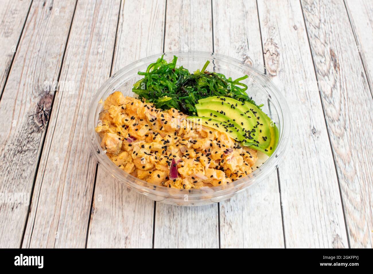 Salmone flambé con cipolla rossa e semi di sesamo. Insalata di alghe di wakame con fette di avocado su una ciotola trasparente in plastica Foto Stock
