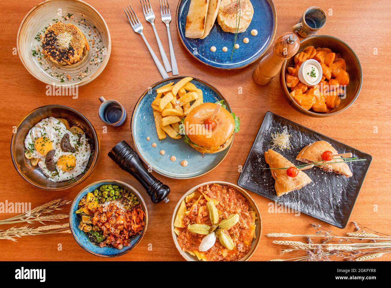 Set di stupendi piatti in ceramica con uova rotte con salsa al tartufo, nachos con guacamole, patatas bravas, ciotola di poke al salmone hawaiano, edamame. Spuntini Foto Stock