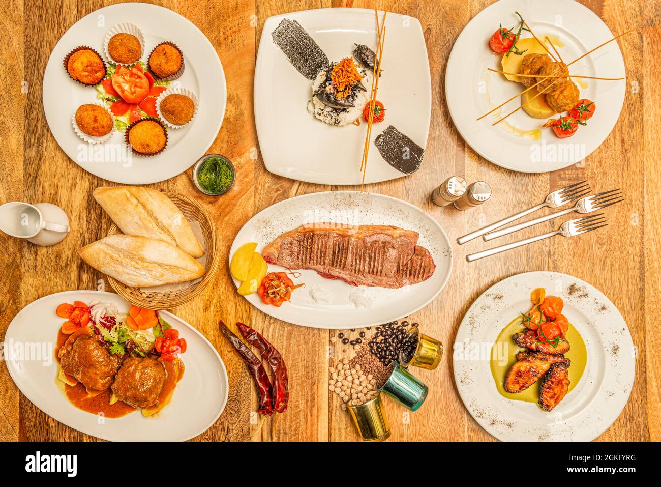 Set di piatti tradizionali spagnoli. Calamari con riso bianco, polpettone con patate, entrecote alla griglia, ali barbecue con pomodori ciliegie Foto Stock