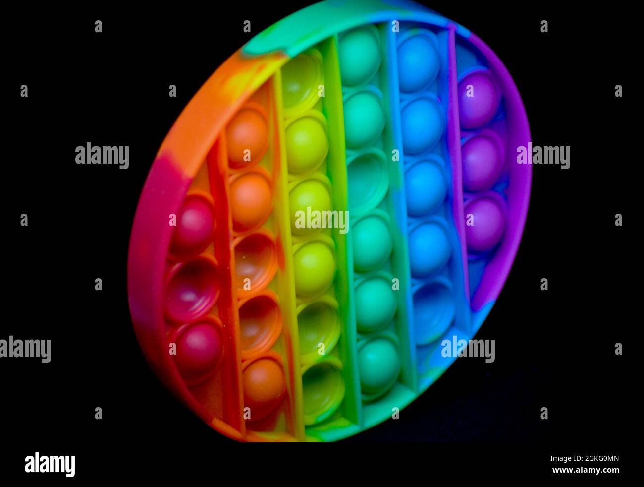 Giocattolo di popper di fedget color arcobaleno per aiutare ad alleviare l'ansia o le difficoltà sensoriali nei bambini. L'immagine viene impostata su uno sfondo nero Foto Stock
