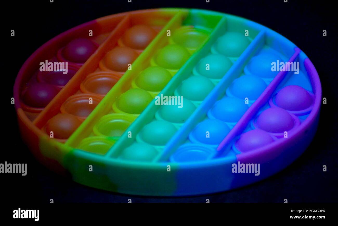 Giocattolo di popper di fedget color arcobaleno per aiutare ad alleviare l'ansia o le difficoltà sensoriali nei bambini. L'immagine viene impostata su uno sfondo nero Foto Stock