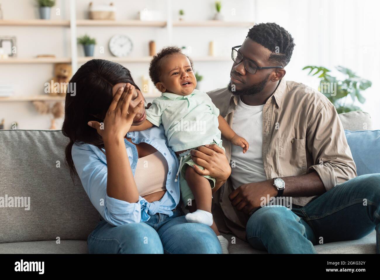 I genitori neri stanchi seduti con il bambino piangendo sul divano Foto Stock