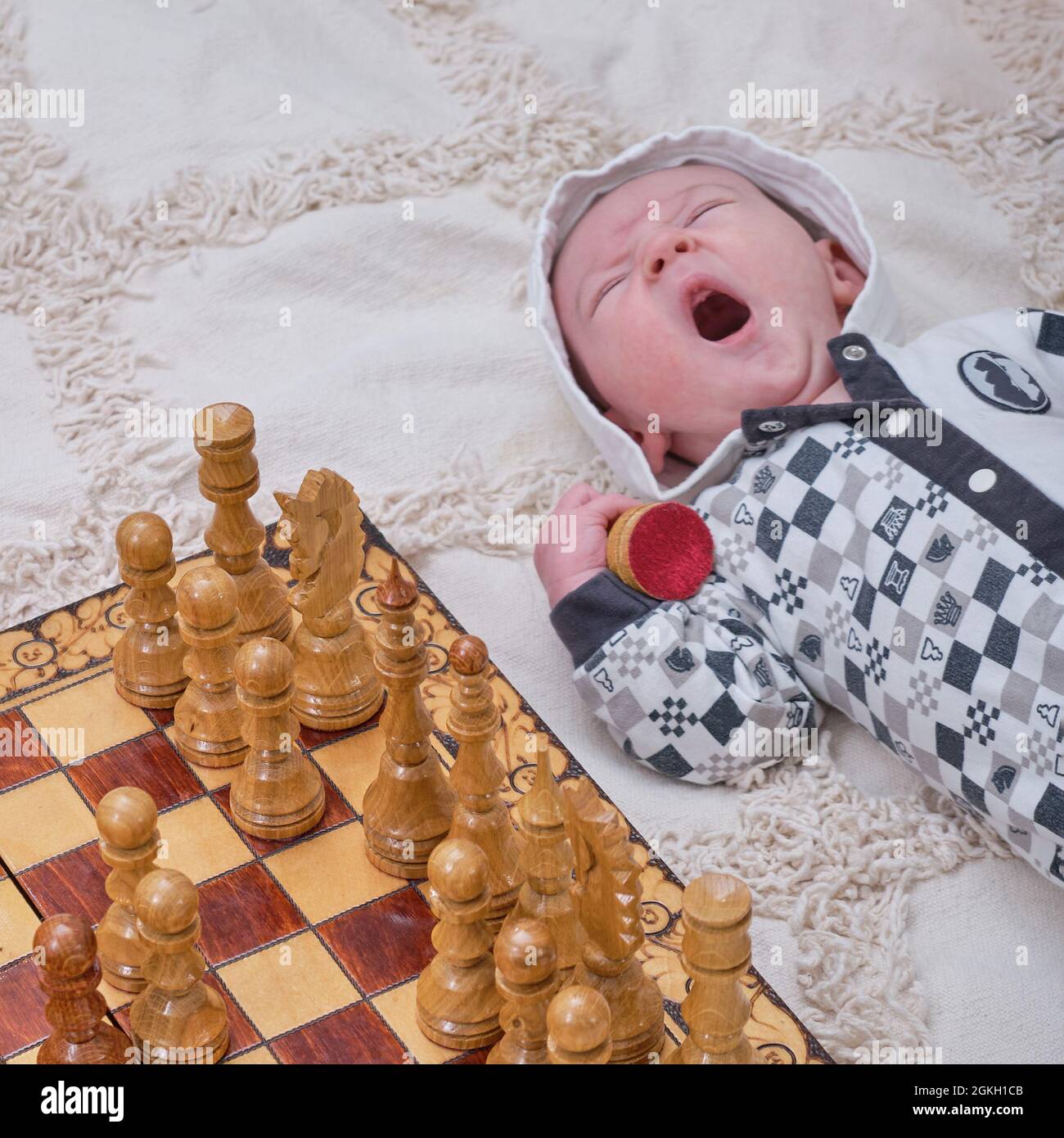 Bambino neonato in una muta a scacchi vicino a una scacchiera con pezzi  messi Foto stock - Alamy