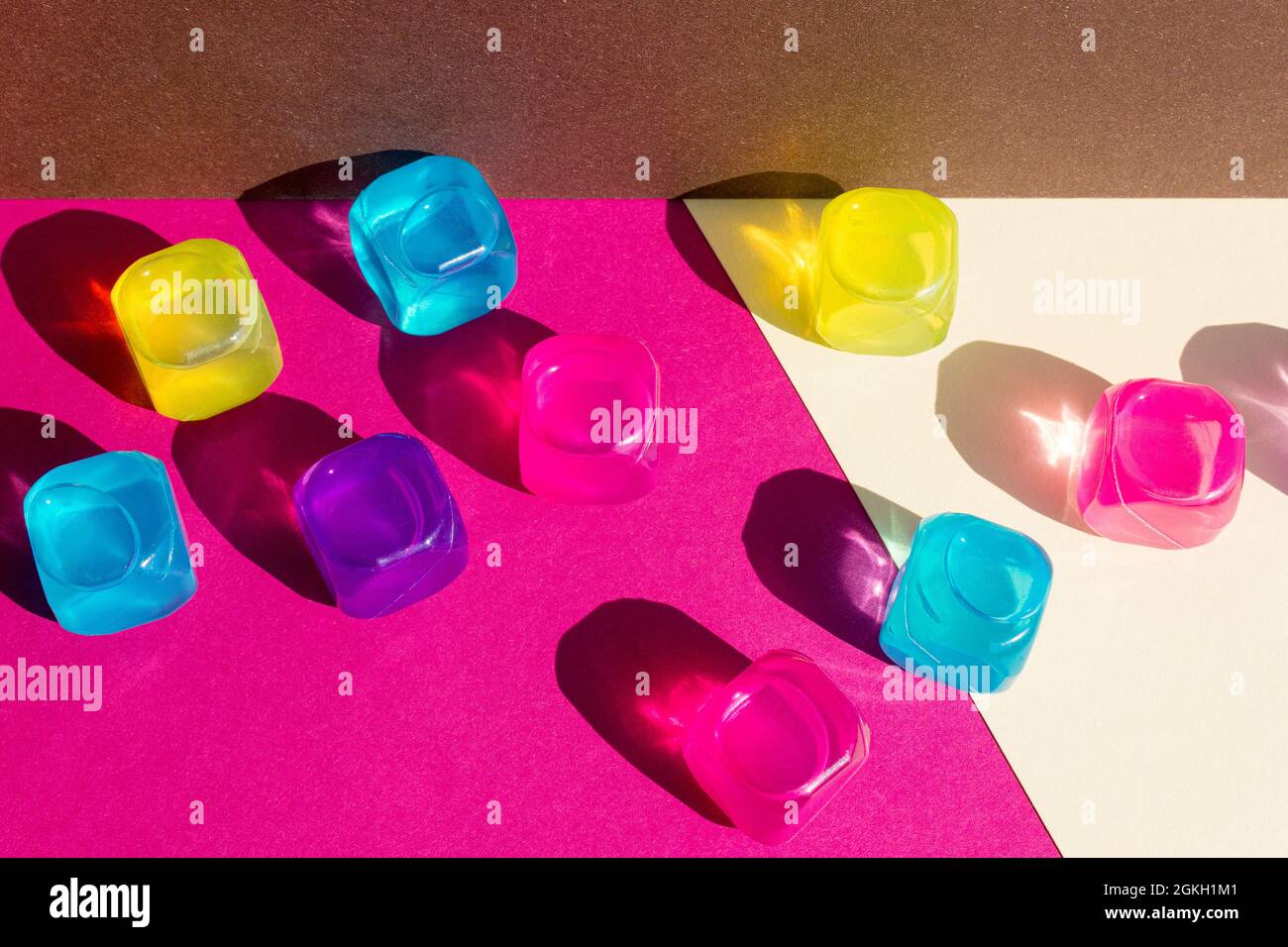 Layout creativo con colorati cubetti di ghiaccio in plastica al sole di mezzogiorno e ombre dure sullo sfondo. Estate mockup. Disposizione piatta. Foto Stock