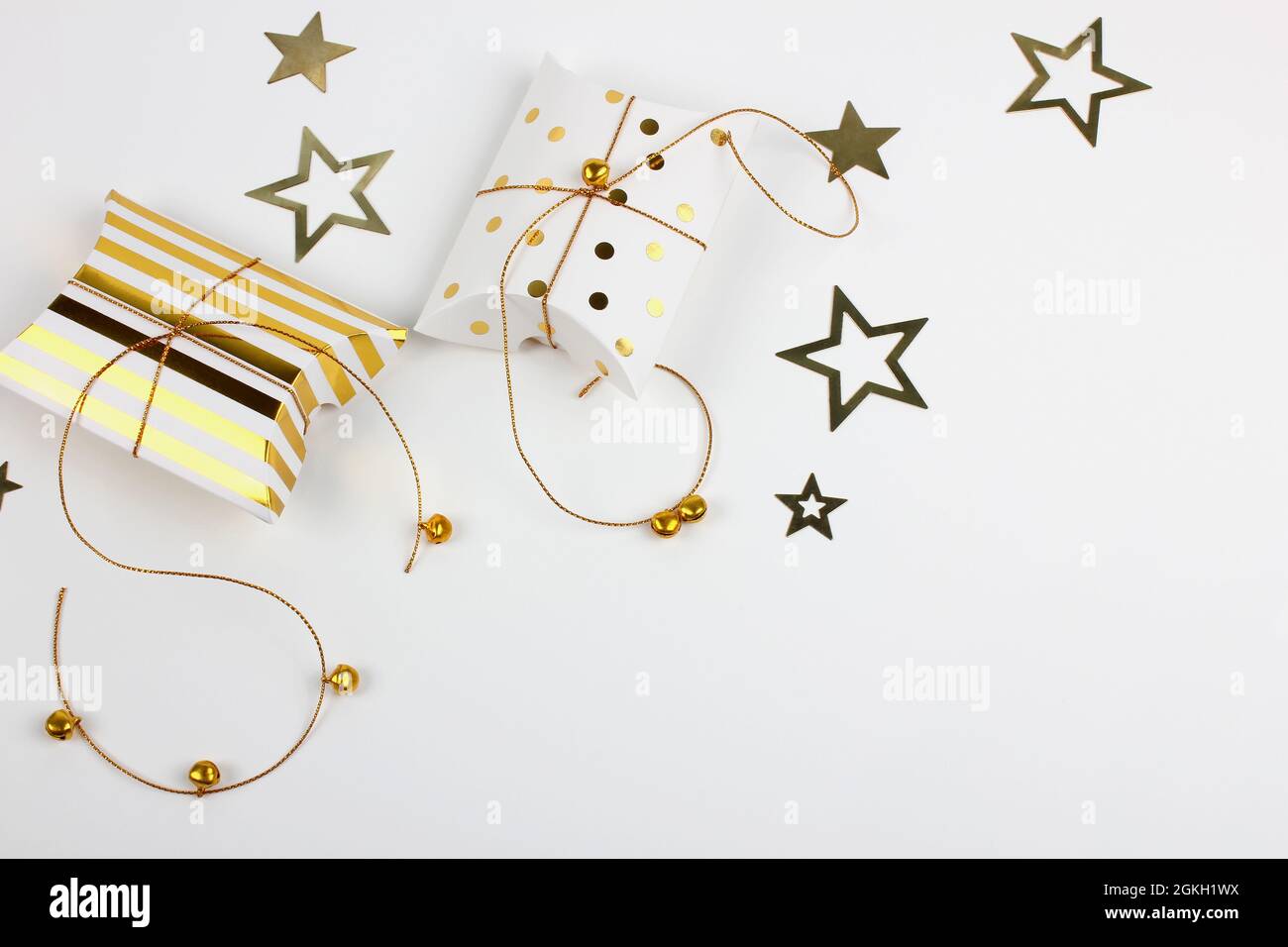 Due confezioni regalo con campane dorate e stelle su sfondo bianco. Buon Natale e Capodanno concetto. Biglietto di auguri. Spazio di copia. Disposizione piatta. Foto Stock