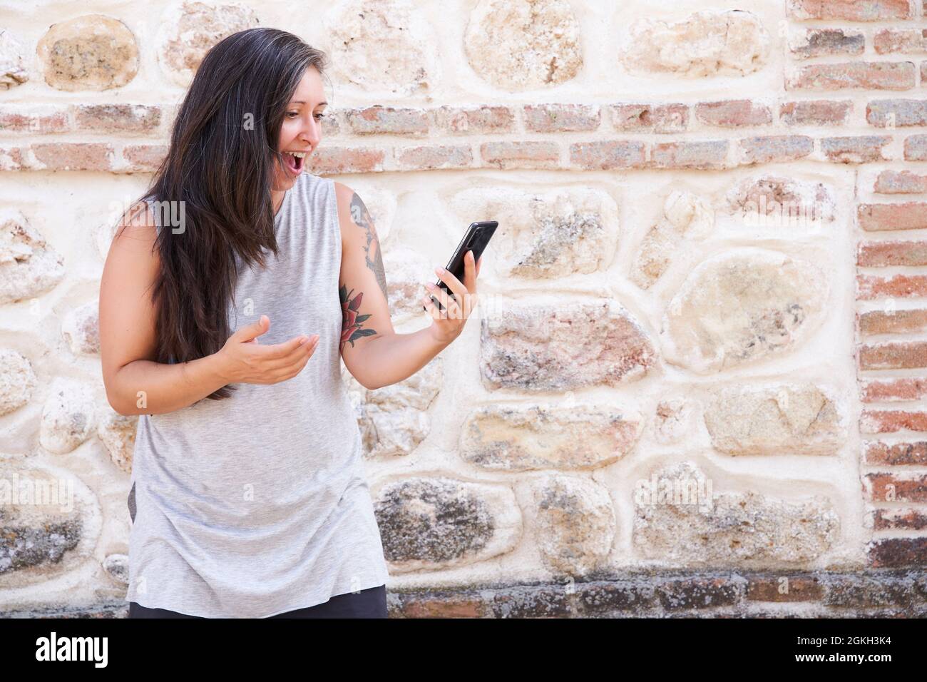 Ragazza scioccata guardando lo schermo del telefono con la bocca aperta. Ritratto all'aperto di una giovane ragazza sorpresa con capelli lunghi indossando un abito casual e holdin Foto Stock