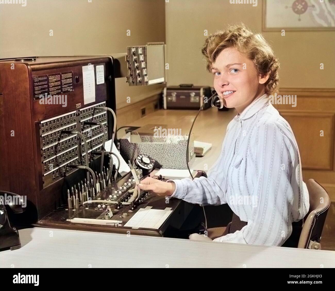 1950 SORRIDENTE DONNA UFFICIO TELEFONO CENTRALINO OPERATORE RECEPTIONIST GUARDARE LA FOTOCAMERA - T2031C HAR001 HARS RITRATTI GROWNUP COMUNICAZIONE SPAZIO COPIA DONNE DI MEZZA LUNGHEZZA PERSONE CRESCIUTE-UP PANNELLO DI PROFESSIONE EYE CONTATTO QUADRO DI CONTROLLO ABILITÀ OCCUPAZIONE FELICITÀ ABILITÀ OPERATORE ALLEGRO SERVIZIO CLIENTI NETWORKING CARRIERE LAVORO OCCUPAZIONI TELEFONI SORRISI CONNESSIONE TELEFONI AMICHEVOLE GIOIOSO DIPENDENTE PIACEVOLE COMUNICARE COMUNICAZIONI GIOVANE ADULTA DONNA CAUCASICA ETNIA HAR001 VECCHIO STILE Foto Stock