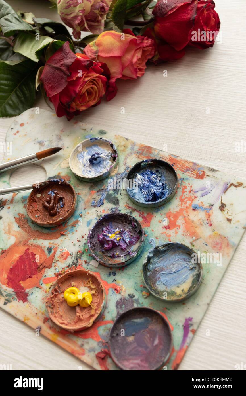 scrivania con tavolozza piena di colori, pennello e bouquet di rose colorate, oggetti d'arte e decorazione, studio Foto Stock