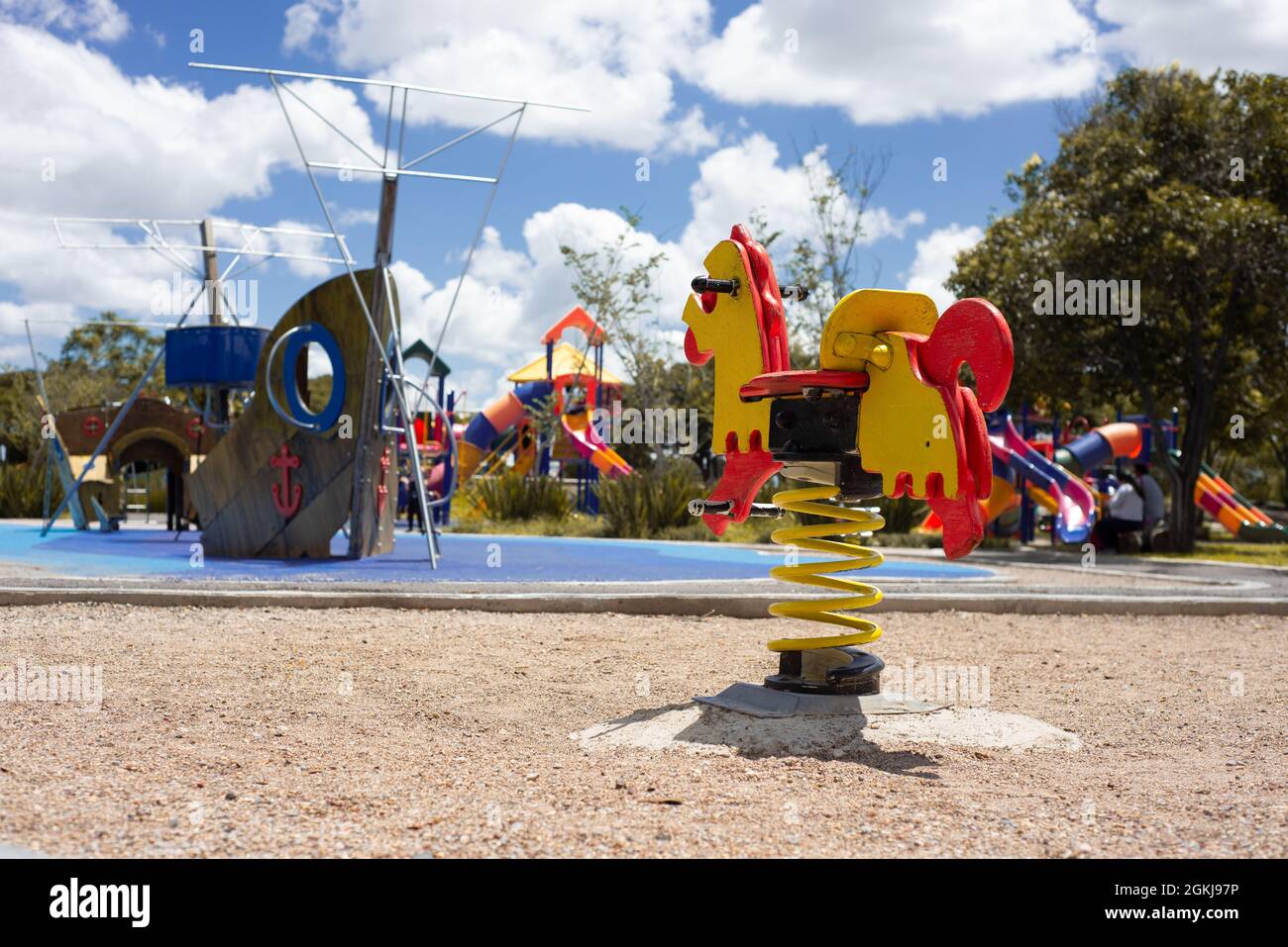 area giochi per bambini all'interno di un parco con alberi, giochi a forma di barca e scivoli, piccolo sedile a forma di cavallo con primavera, senza persone Foto Stock