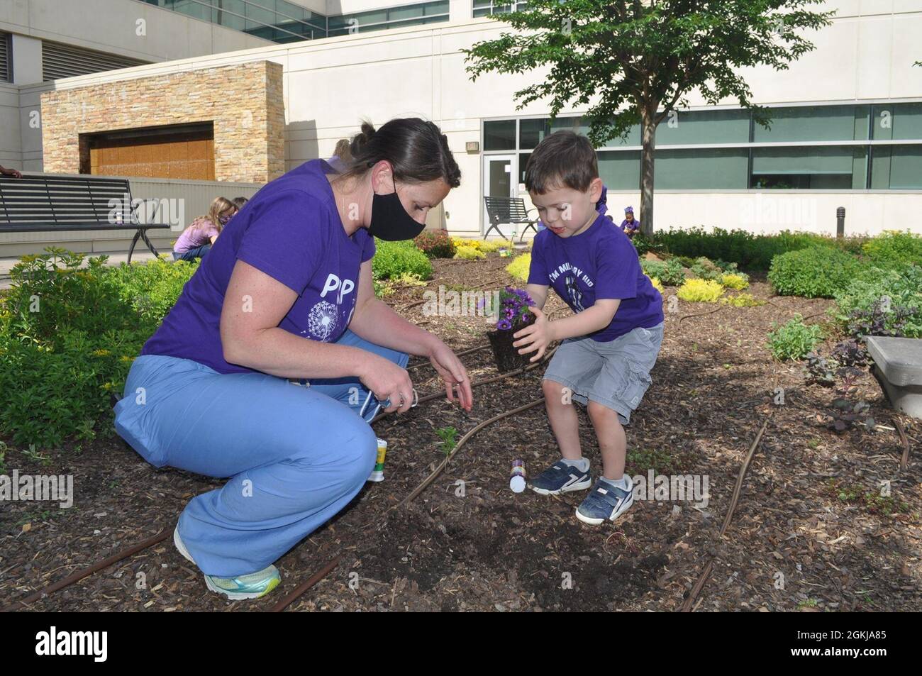 Jessica Aguilar pianta un fiore viola con suo figlio Axel come parte del mese di BMACH della celebrazione militare del bambino. Foto Stock