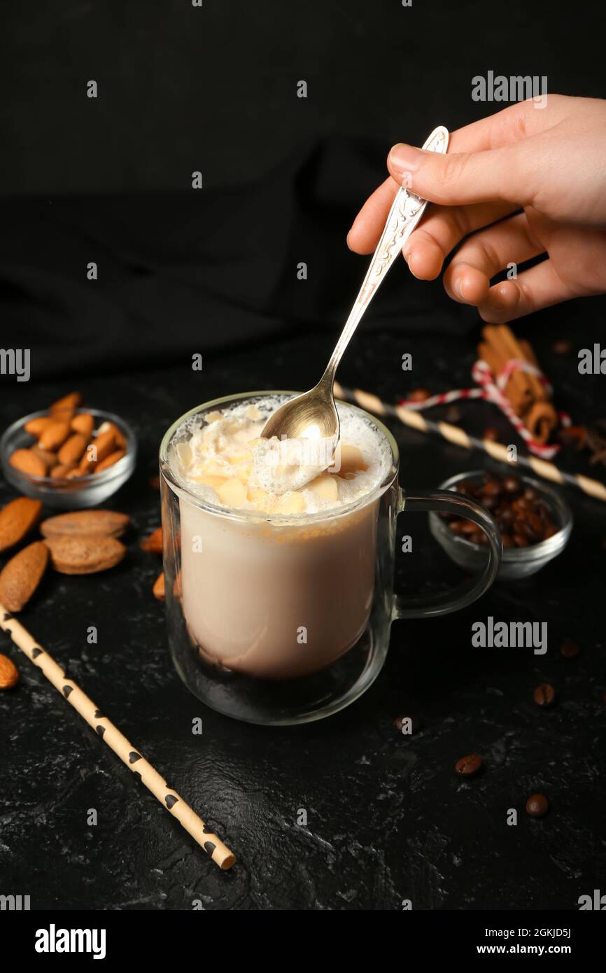 Donna che mescola gustoso latte di mandorle in bicchiere su sfondo scuro Foto Stock