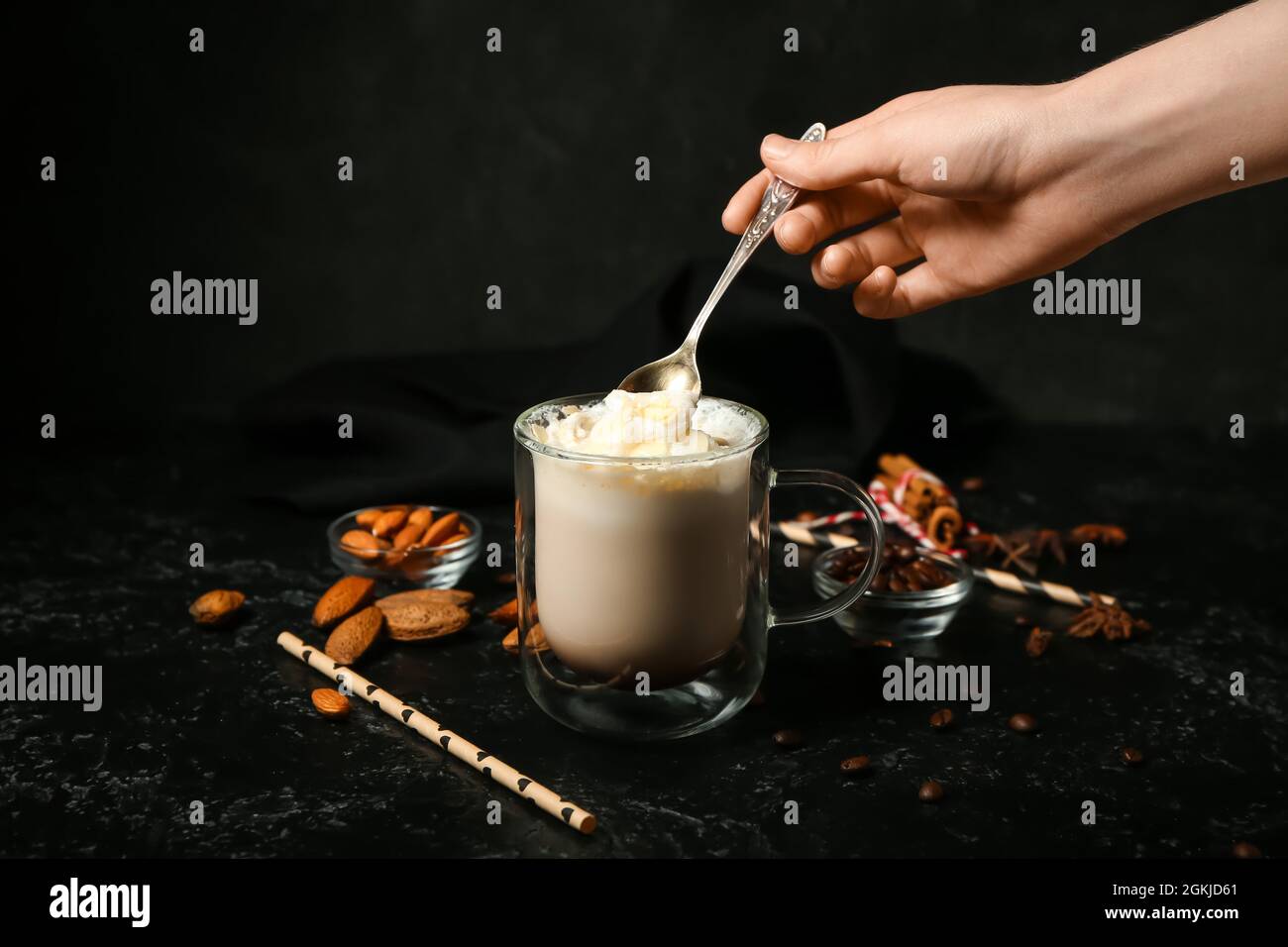 Donna che mescola gustoso latte di mandorle in bicchiere su sfondo scuro Foto Stock