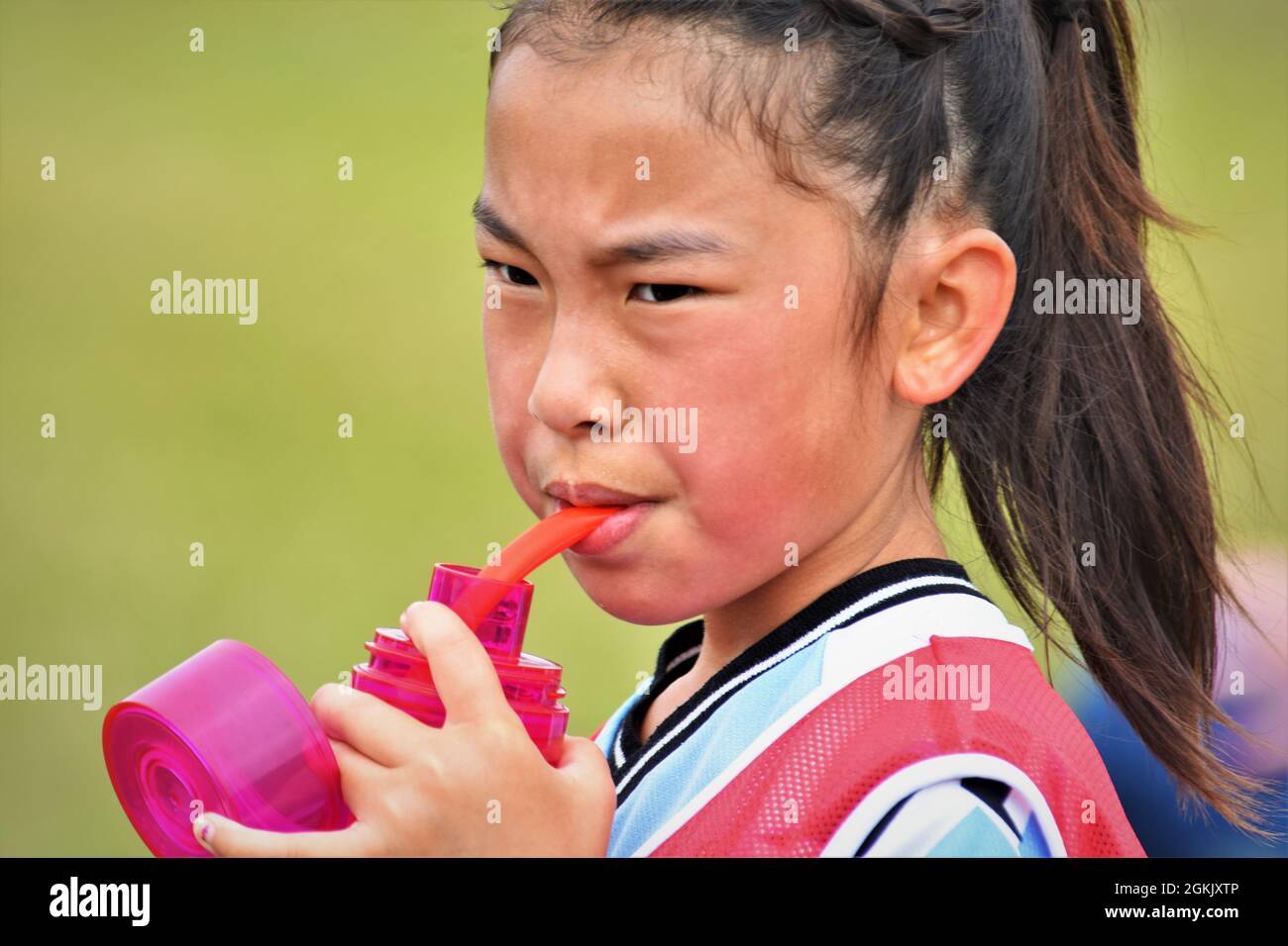 Giovane ragazza asiatica a metà tempo del suo gioco di calcio con bottiglia d'acqua e coda di pony Foto Stock