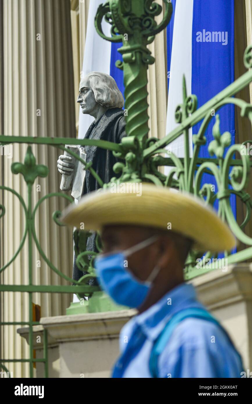 San Salvador, El Salvador. 14 settembre 2021. Un uomo indigeno si erge accanto a una statua raffigurante Cristoforo Colombo al Palazzo Nazionale, durante la dimostrazione. I membri della comunità indigena Nahuizalco protestano contro la Giornata dell'Indipendenza Bicentenaria di El Salvador, definendola indipendenza per i ricchi. Il 15 settembre l'America Centrale commemora il 200° anniversario dell'Indipendenza dalla Spagna. Credit: SOPA Images Limited/Alamy Live News Foto Stock