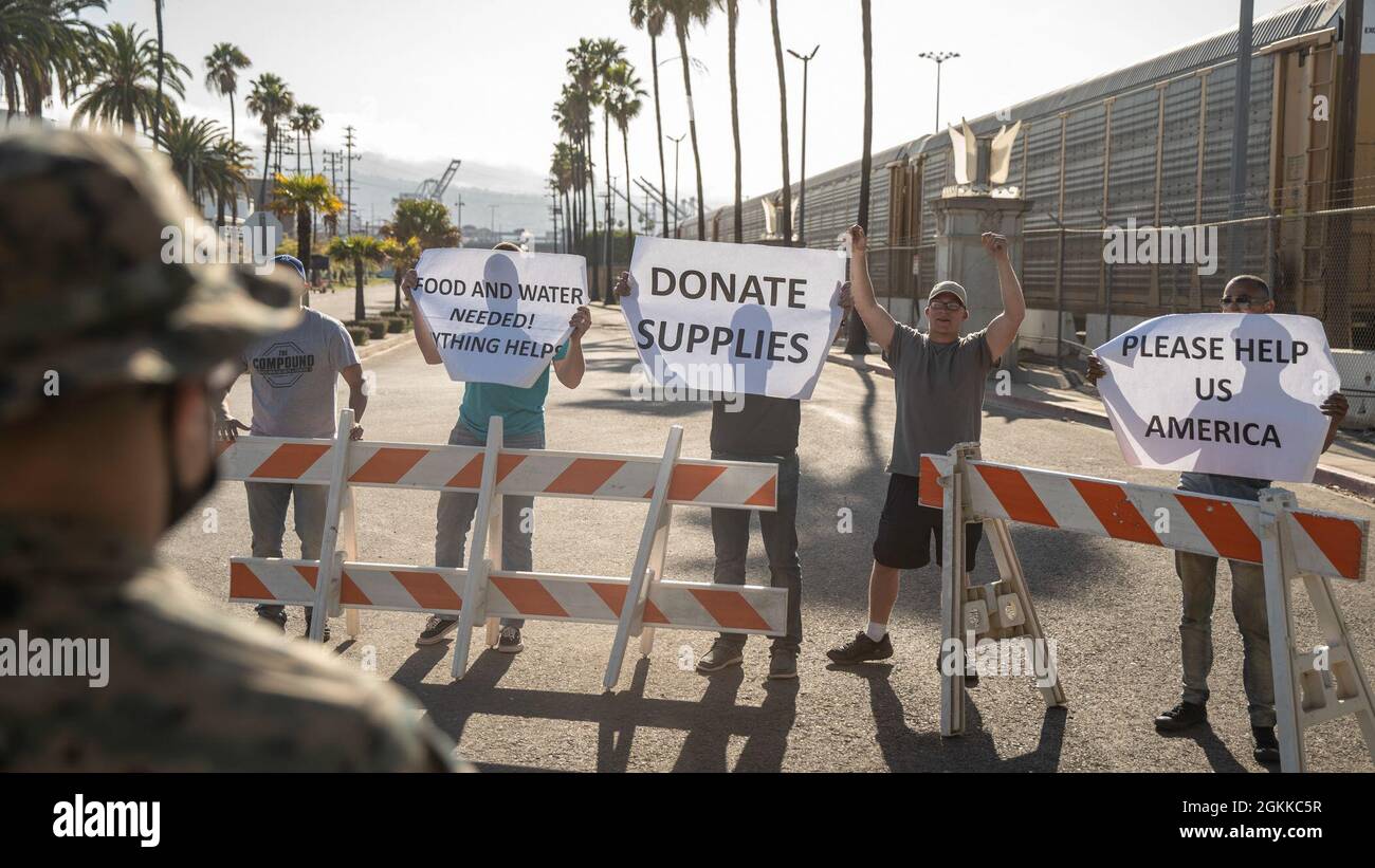 LONG BEACH, California (14 maggio 2021) Un Marina degli Stati Uniti con Charlie Company, Battalion Landing Team 1/1, 11th Marine Expeditionary Unit (MEU), osserva i cittadini locali simulati che protestano durante un esercizio di rafforzamento delle ambasciate, maggio 14. Marines e marinai dell'Essex Amphibious Ready Group (ARG) e dell'XI MEU stanno conducendo allenamenti di routine sulle e al largo delle coste della California meridionale. Foto Stock