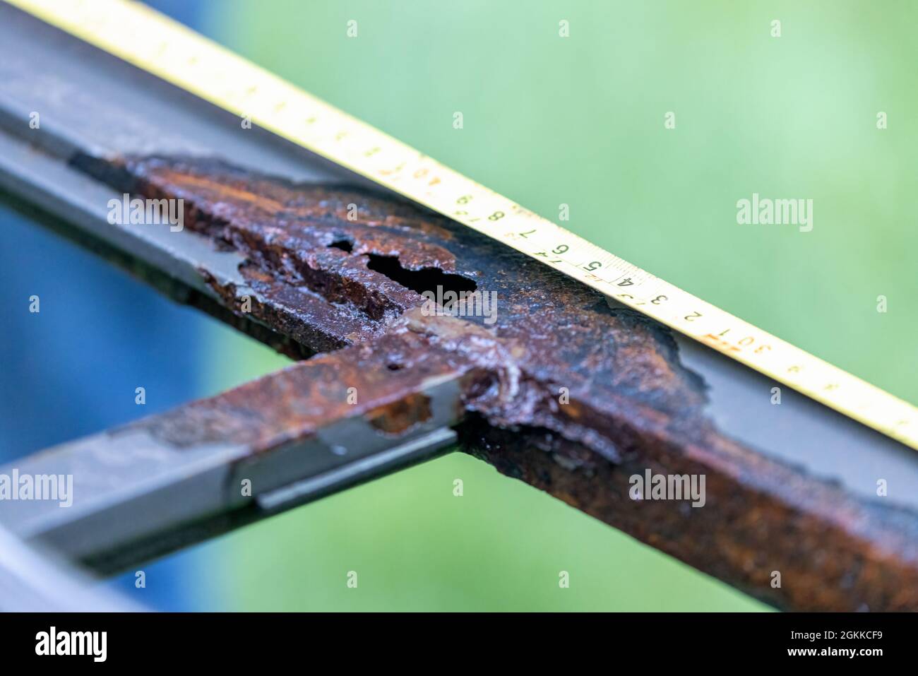 telaio in metallo vecchio corroso con foro per danni causati dall'acqua misurato con nastro di misurazione giallo Foto Stock