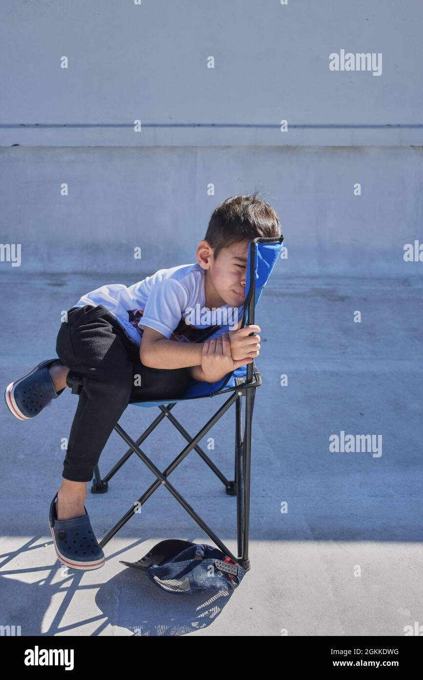 ragazzo bruna arrabbiato sdraiato su una sedia a sdraio blu, appoggiando il  viso contro la schiena della sedia. vista frontale. estate. orizzontale  Foto stock - Alamy