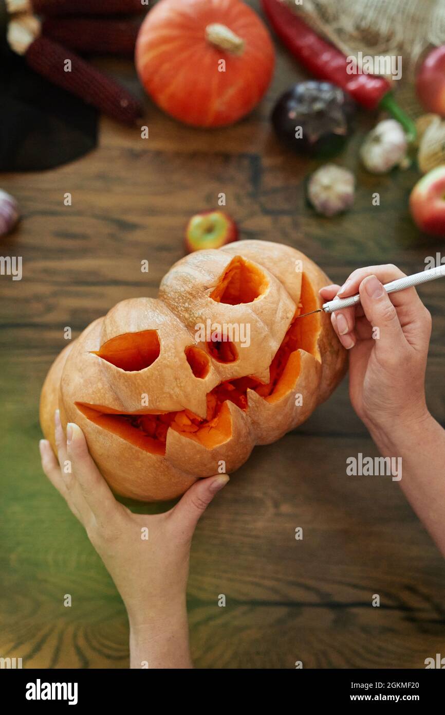 Donna mani scultura di zucca o Halloween concetto. Vista dall'alto della zucca come tradizione stagionale autunnale. La donna fa un occhio in una zucca per fare un jack o'lantern su un tavolo di legno. Immagine di alta qualità Foto Stock