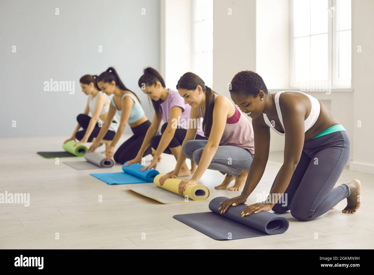 Gruppo di donne che arrotolano i tappetini in gomma dopo un allenamento di fitness o una lezione di yoga in palestra Foto Stock