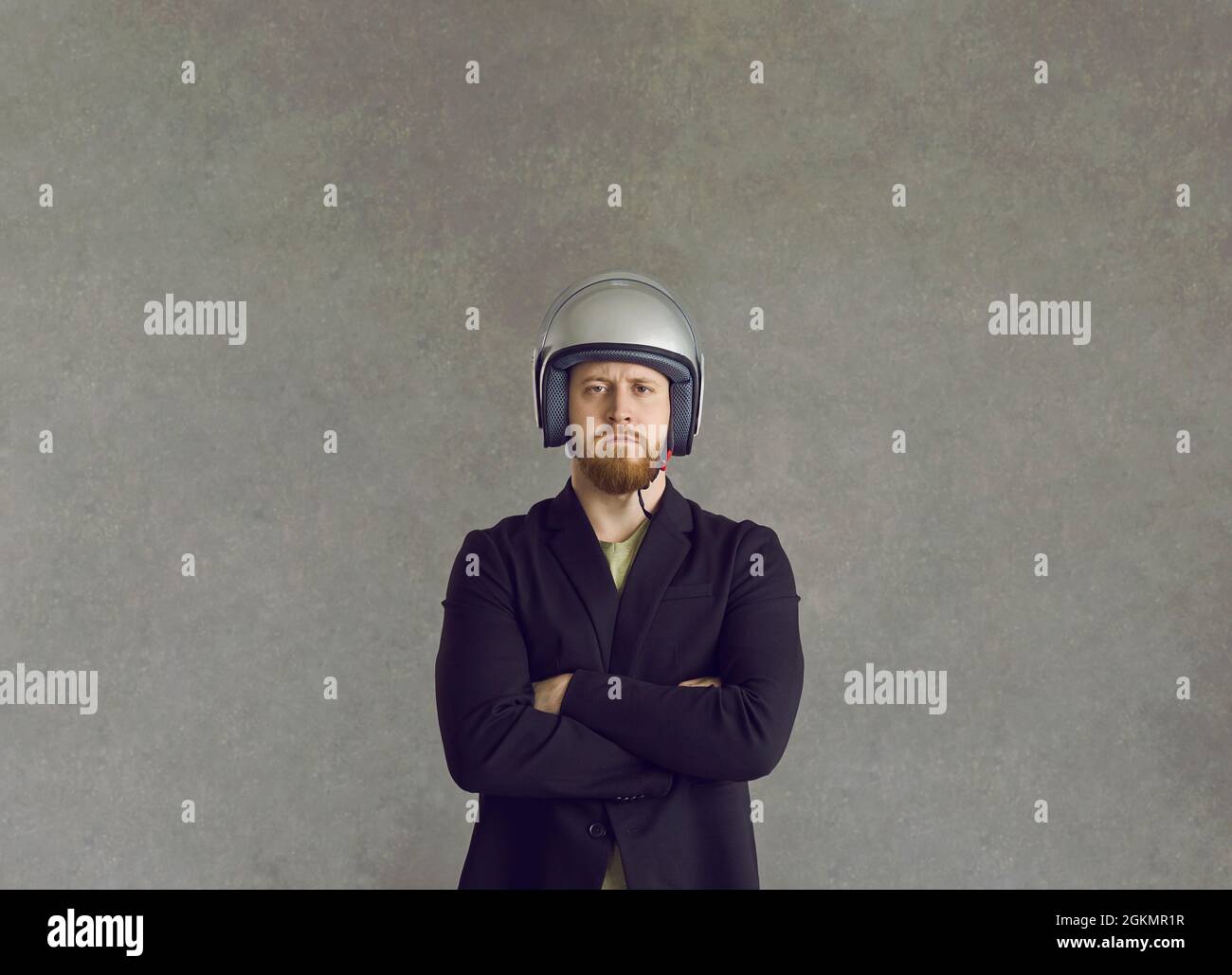 Uomo serio in tuta e casco braccia in piedi ripiegate su sfondo grigio studio Foto Stock
