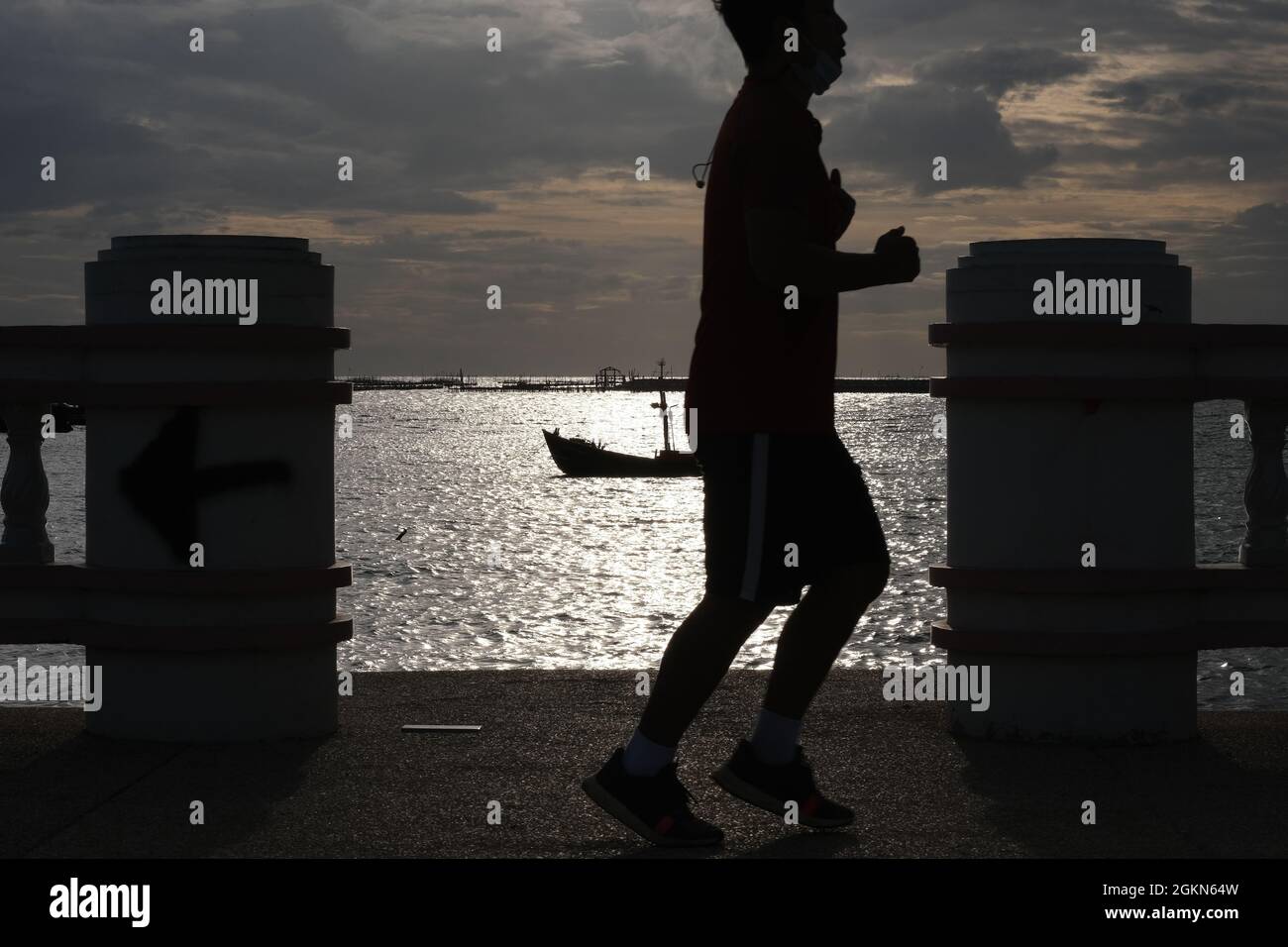 Una silhouette di uomo che fa jogging contro il mare illuminato dal sole Foto Stock