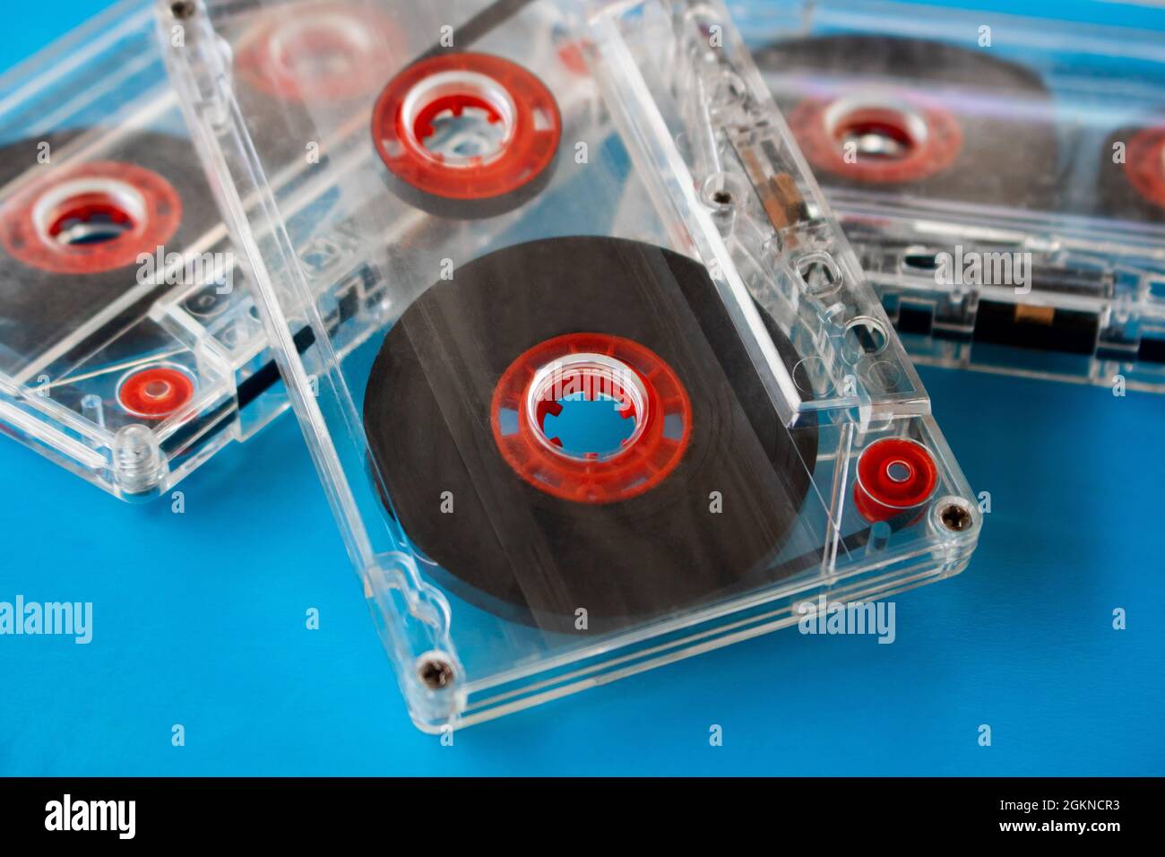 Diverse cassette audio compatte trasparenti con nastro visibile e bobine interne rosse poste casualmente su sfondo blu. Tecnica di messa a fuoco selettiva Foto Stock