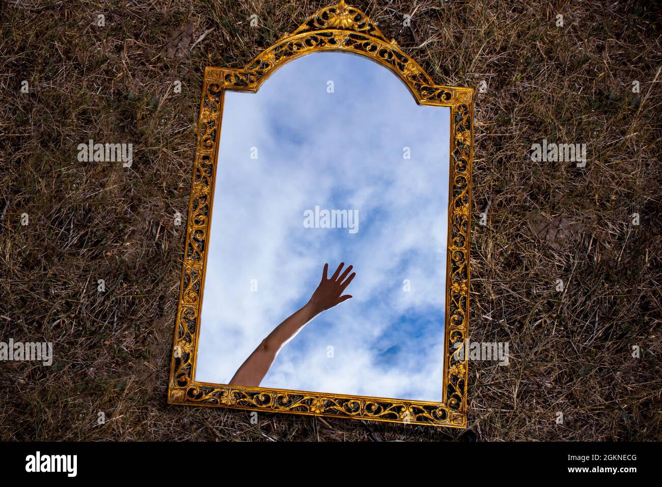 Specchio dorato vintage adagiato su sfondo scuro che riflette una mano misteriosa che si allunga sopra il cielo blu e le nuvole. Vista dall'alto. Mano d'aiuto Foto Stock