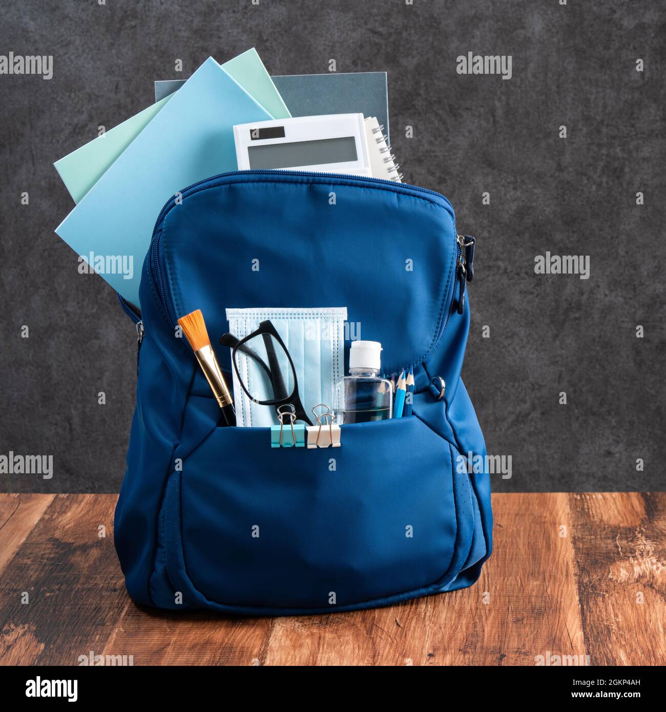Primo piano dello zaino blu con cancelleria della scuola su tavola di legno e sfondo nero, concetto di design di ritorno alla scuola. Foto Stock