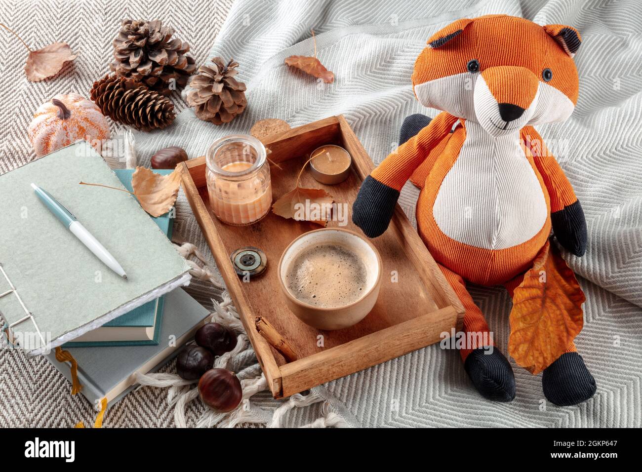 Hygge ancora vita con un giocattolo volpe, una tazza di caffè, foglie d'autunno e un giornale su una coperta calda Foto Stock