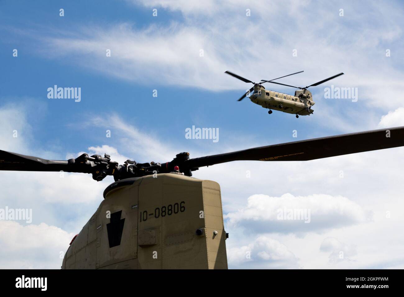 Un elicottero Chinook della Guardia Nazionale degli Stati Uniti CH-47, dal secondo battaglione, 104th Aviation Regiment, vola oltre un elicottero CH-47 Chinook stazionario alla gamma 48, Fort Drum, New York, 13 giugno 2021. CH-47 Chinook elicotteri sono stati nel servizio dell'esercito degli Stati Uniti dal 1962, servendo come elicottero di trasporto. Foto Stock