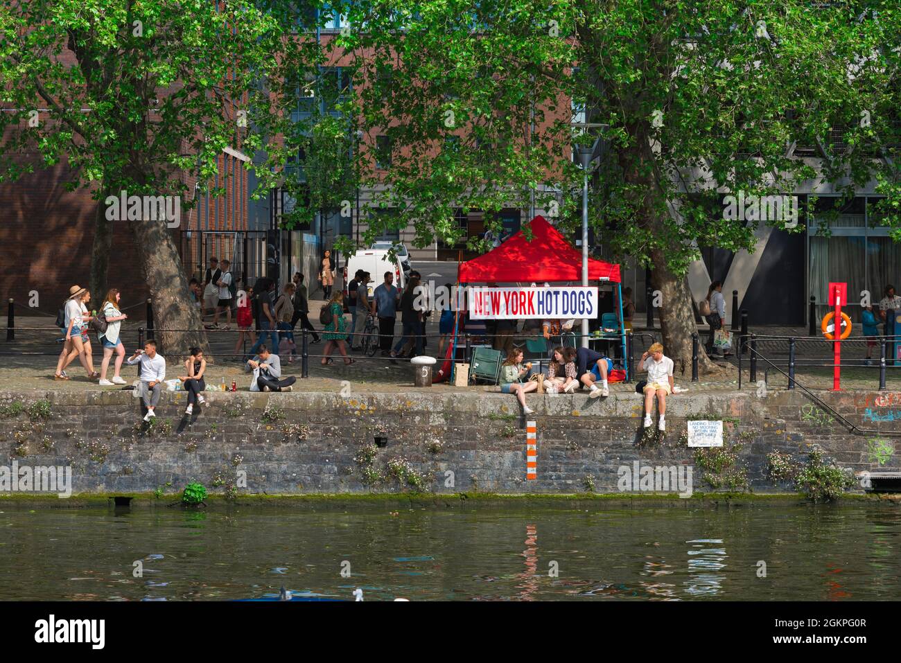 I giovani si rilassano, in estate, si può ammirare la vista dei giovani che si rilassano lungo lo stretto Quay nella storica zona di Harbourside di Bristol, Inghilterra, Regno Unito Foto Stock