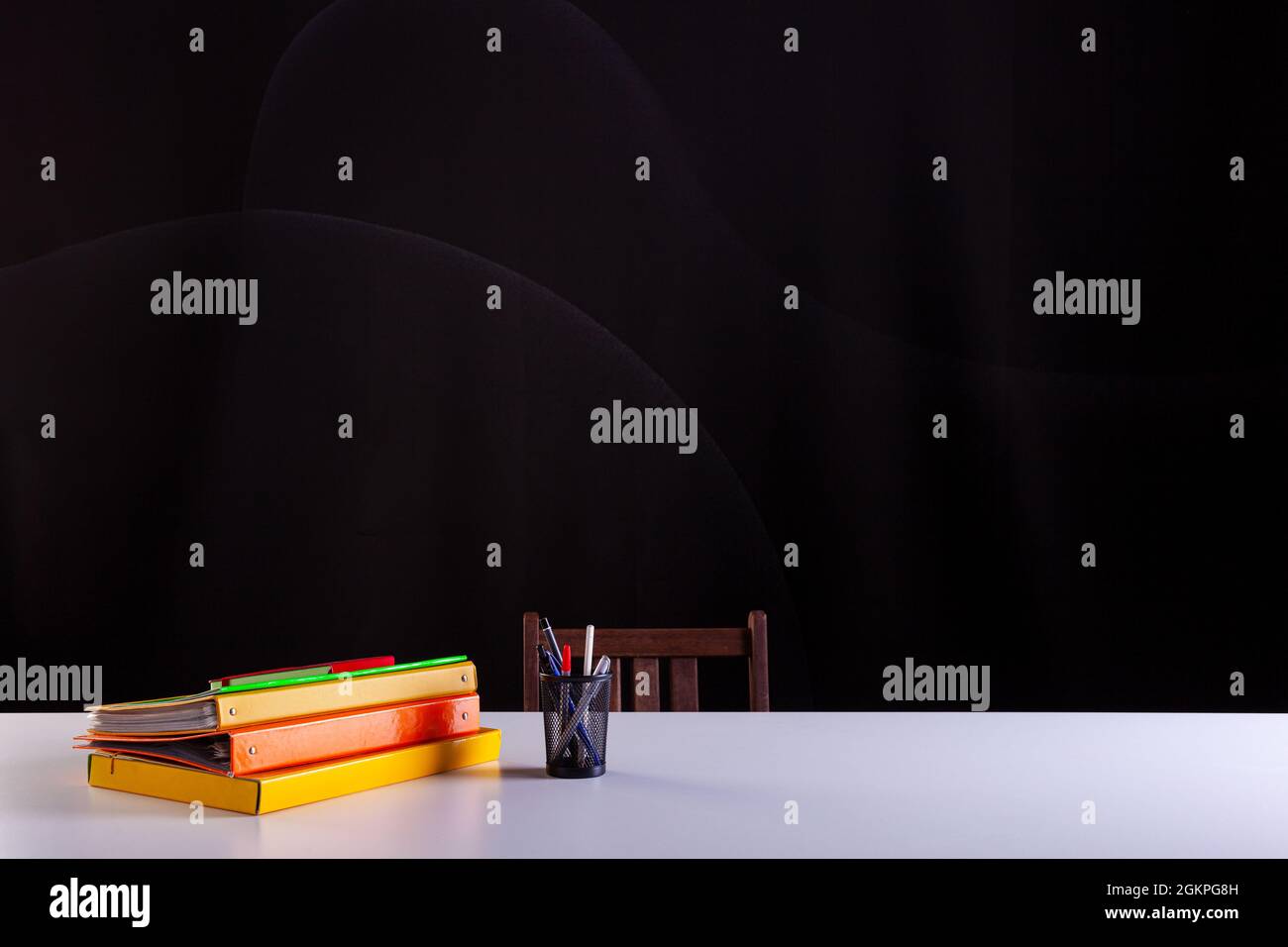 Pentola matite accanto ai libri impilati, forniture scolastiche su scrivania bianca con struttura lavagna in background. Vista laterale, spazio di copia. Apprendimento, istruzione Foto Stock