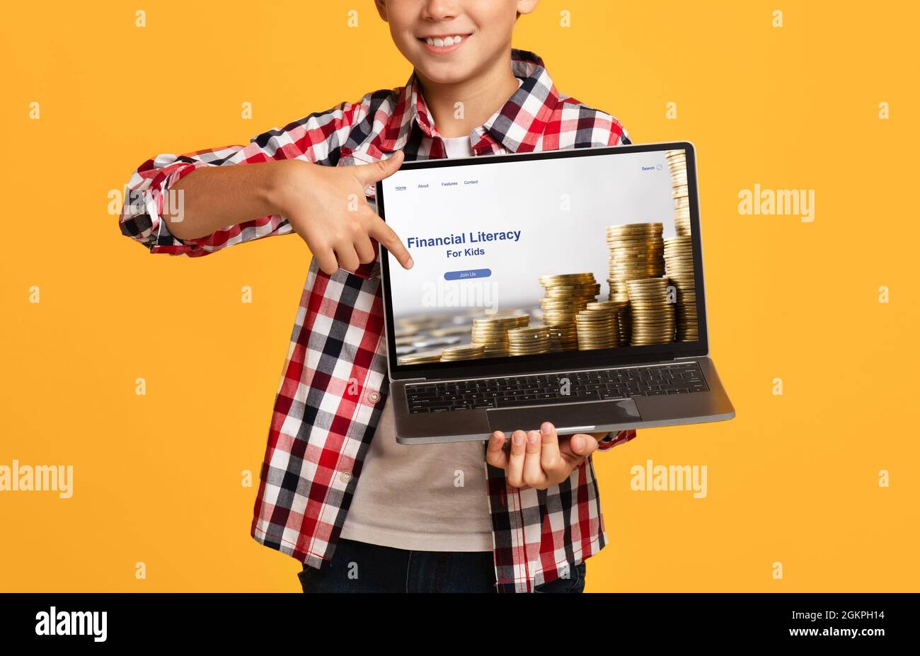 Primo piano del ragazzo felice che punta allo schermo del portatile con il Web site educativo di alfabetizzazione finanziaria per i capretti, sfondo arancione Foto Stock