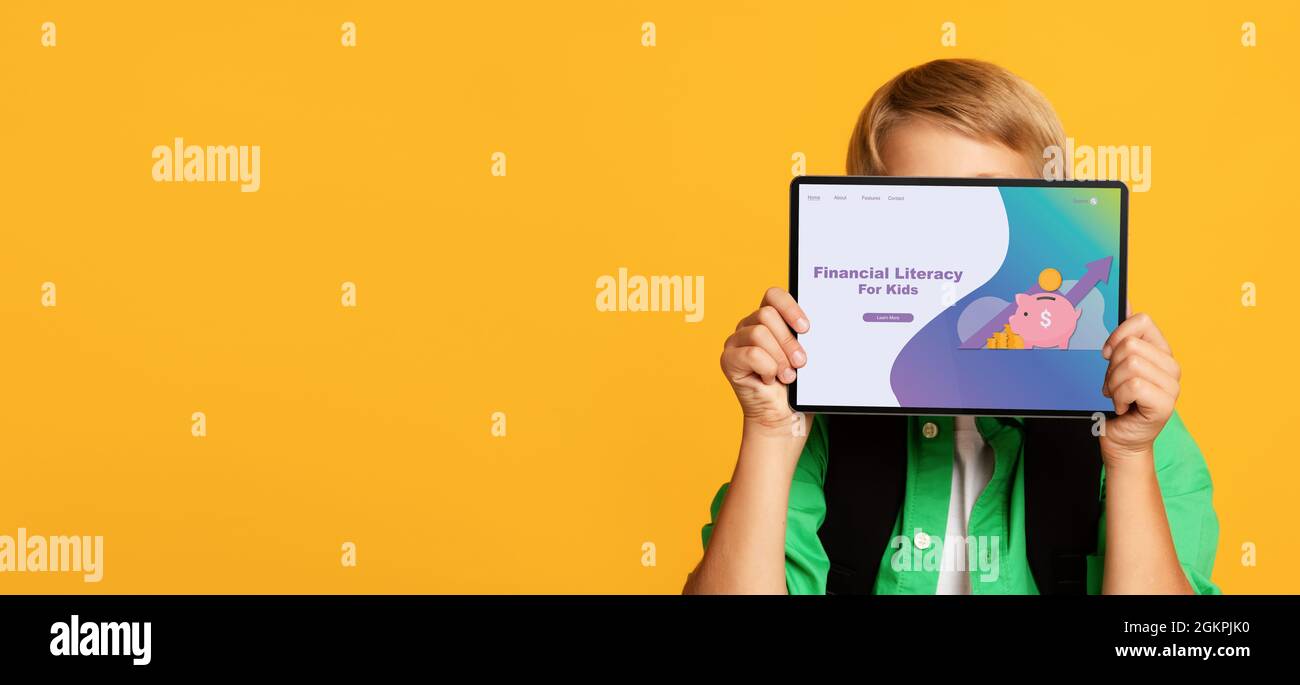 Ragazzo biondo che copre il suo volto con il computer tablet, facendo pubblicità a Financial Literacy for Kids sito web su sfondo arancione Foto Stock