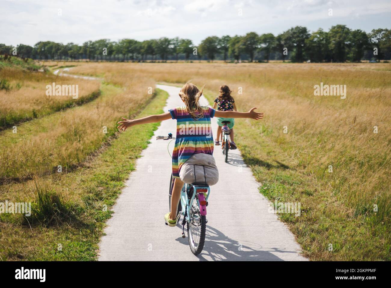 Bambina che guida una bicicletta con le braccia tese Foto Stock