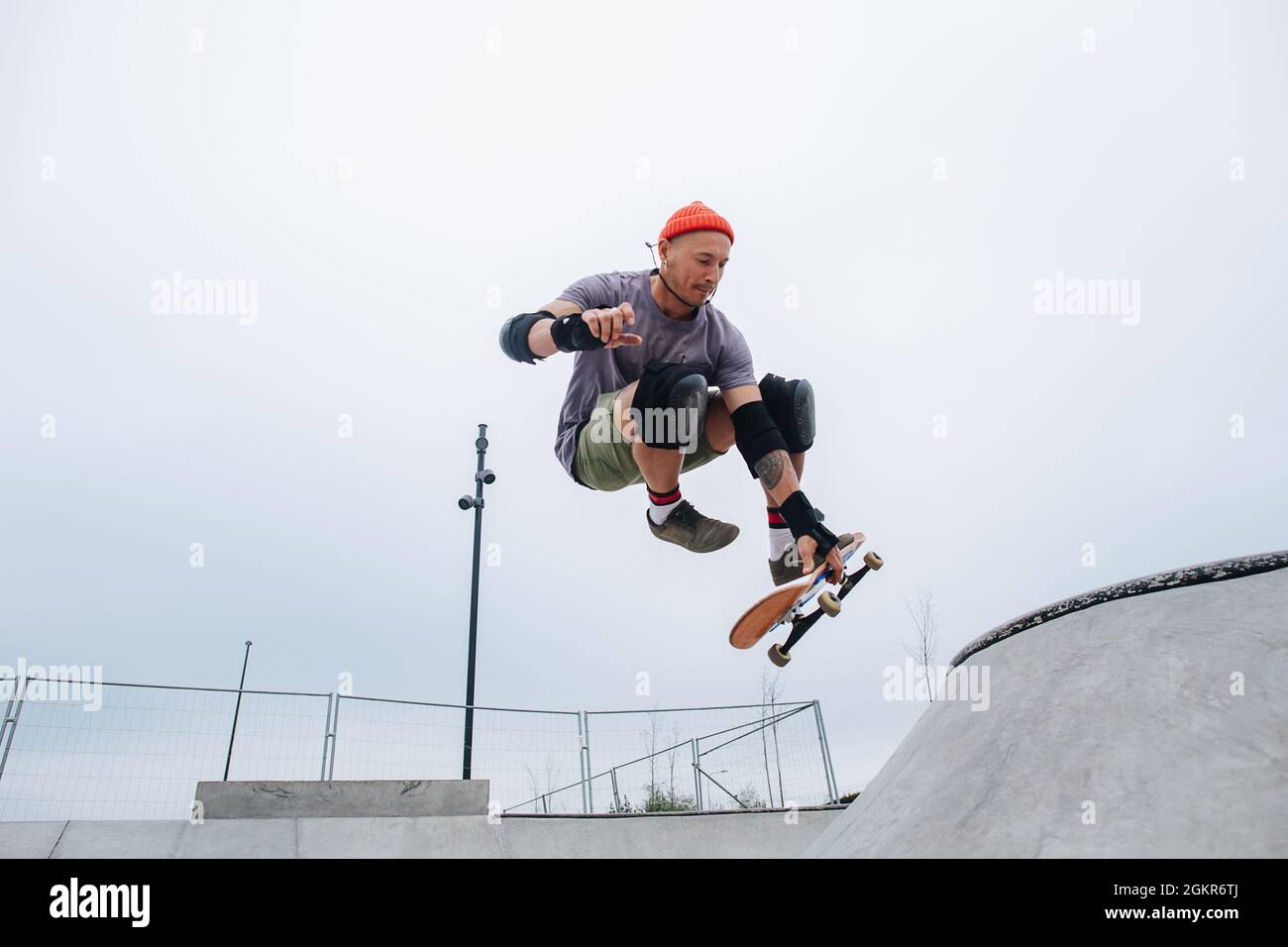 Impressionante skater maturo in una berretto di guardia che inizia il suo lancio, saltando con la sua tavola in un parco di pattini. Angolo verso l'alto, con il hovering nell'aria. Foto Stock