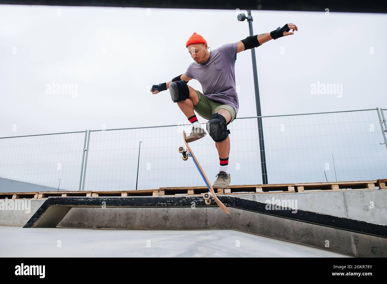 Skater agile e maturo in un cappello da orologio che fa trucchi con uno skateboard su una rampa in un parco skate. Verso l'alto, hovering nell'aria con il bordo ad un an Foto Stock
