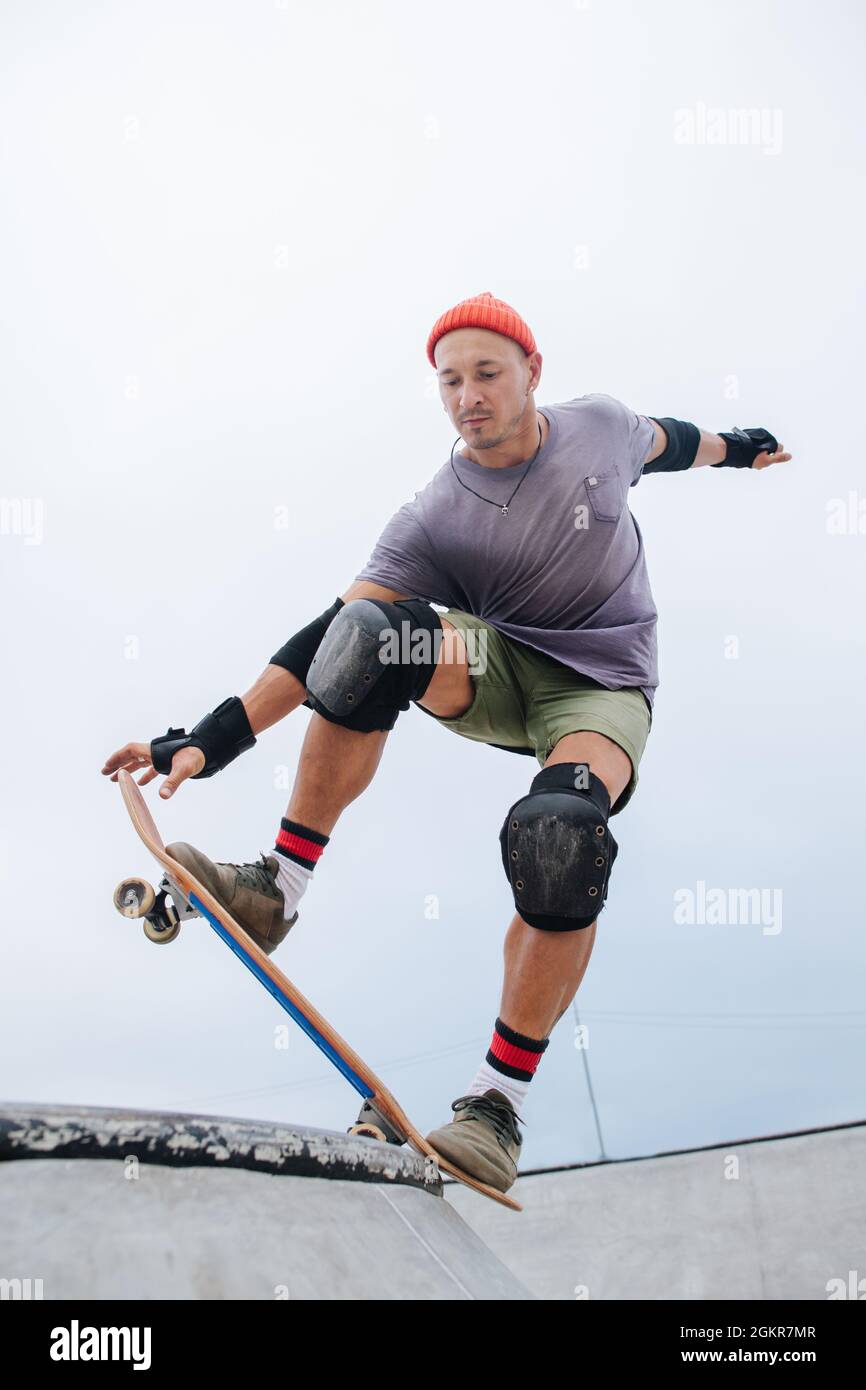 Skater maturo e sicuro in un cappellino da orologio che inizia il suo lancio in un parco skate. Angolo verso l'alto, inclinazione della borra, inclinazione in avanti. Foto Stock