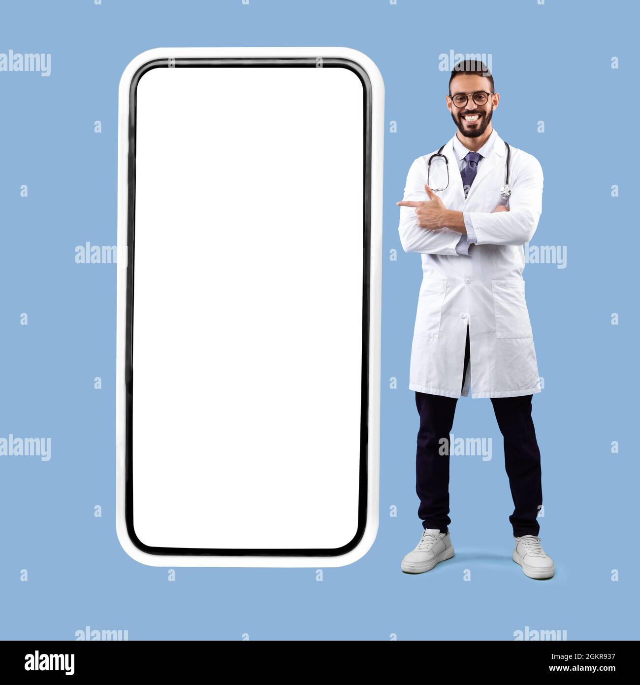 Medico maschio arabo in posa vicino a schermo grande del telefono, sfondo blu Foto Stock