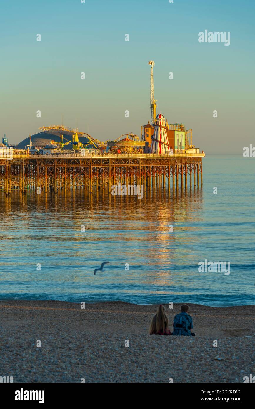 Vista della coppia sulla spiaggia e sul molo del Palazzo di Brighton al tramonto, Brighton, East Sussex, Inghilterra, Regno Unito, Europa Foto Stock