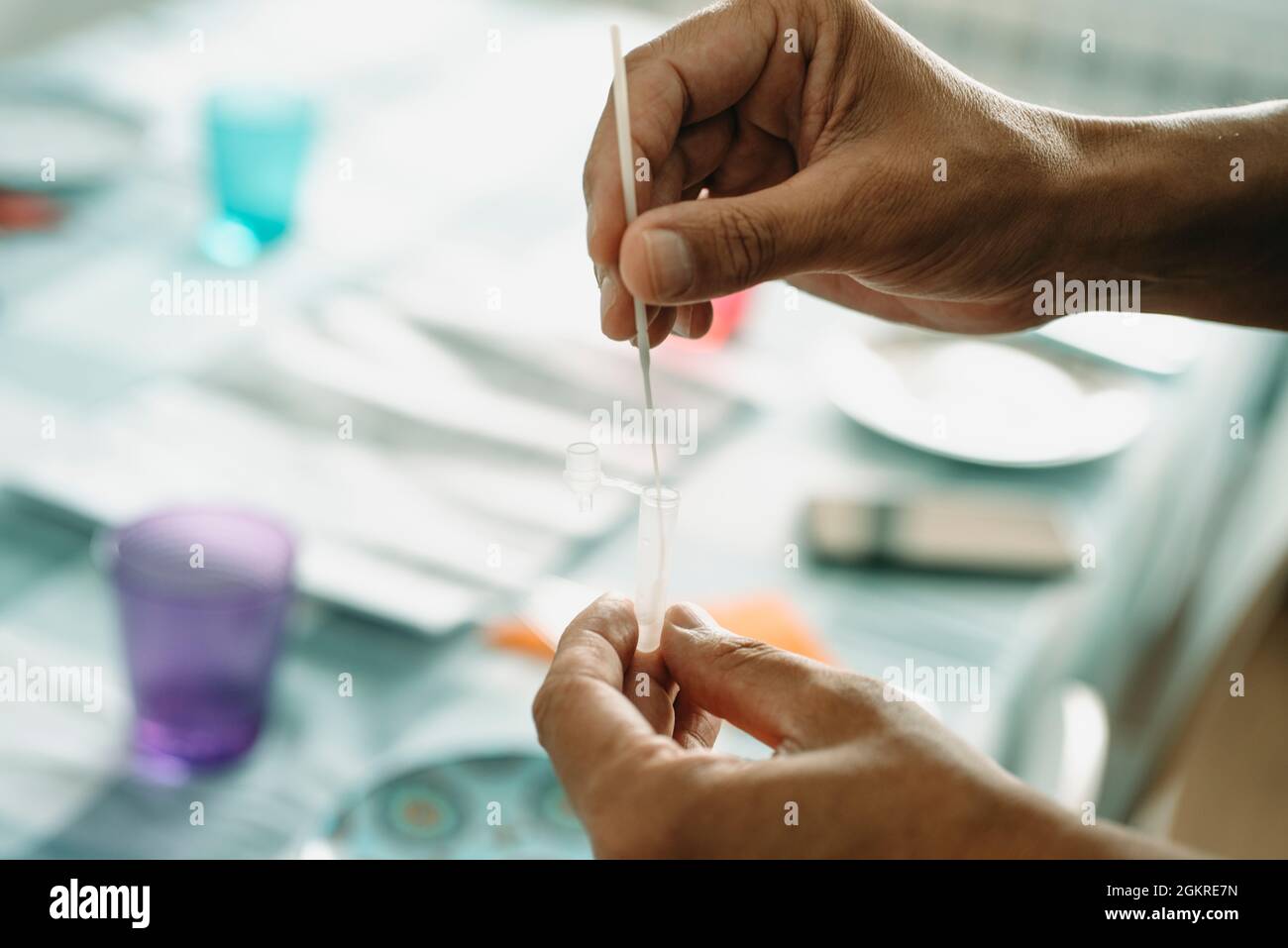 un giovane uomo caucasico pone un tampone nasofaringeo con il proprio campione in una pipetta, come avviene con un test diagnostico dell'antigene covid-19, in un set di tabelle Foto Stock