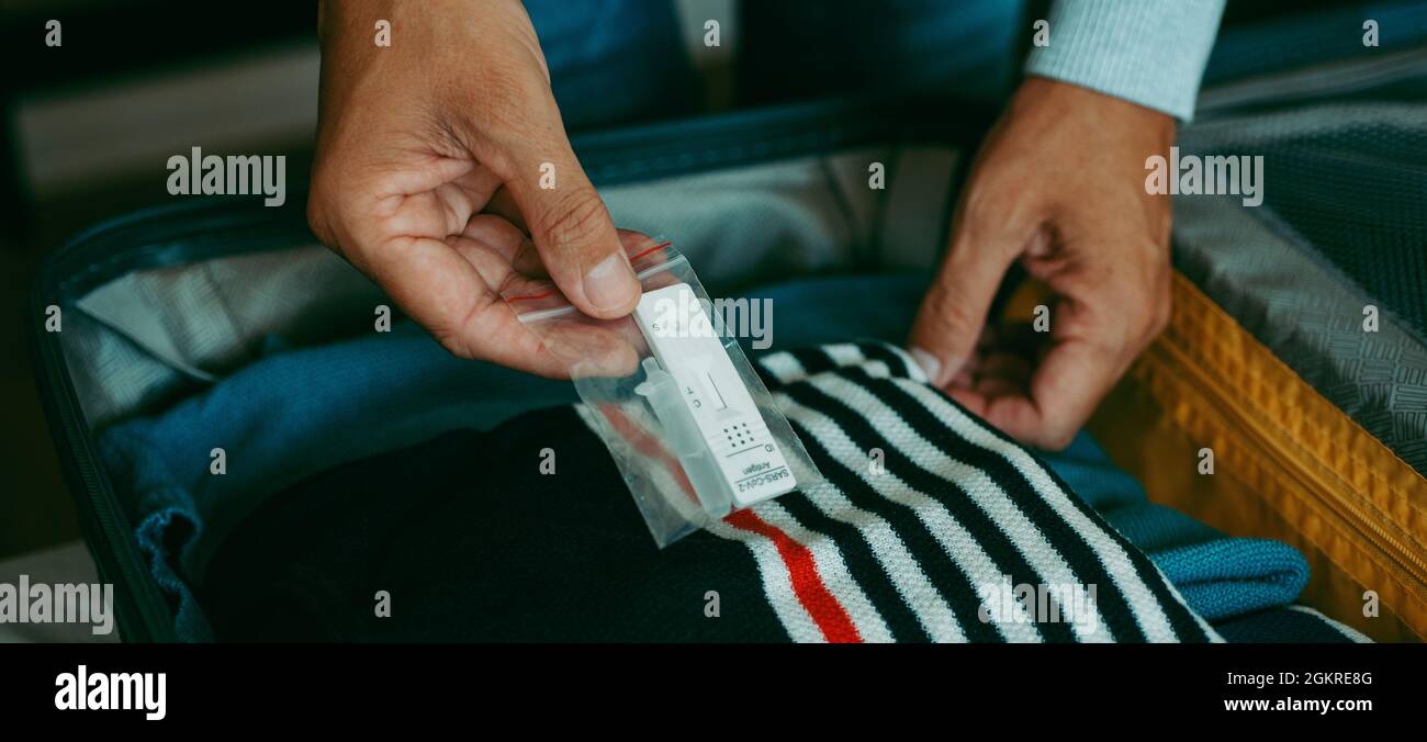 un giovane uomo mette in valigia un covid-19 test diagnostico antigene kit, imballato con diversi vestiti, in un formato panoramico da utilizzare come banner web o. Foto Stock