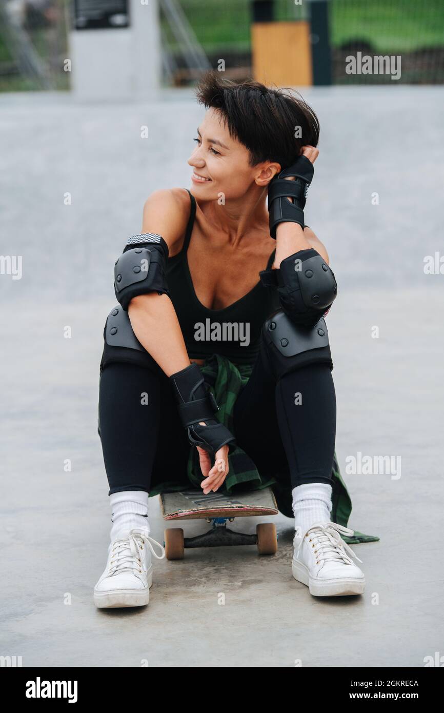 Felice pattinatore donna con capelli corti poggiati sulla sua tavola, godendosi. Foto Stock