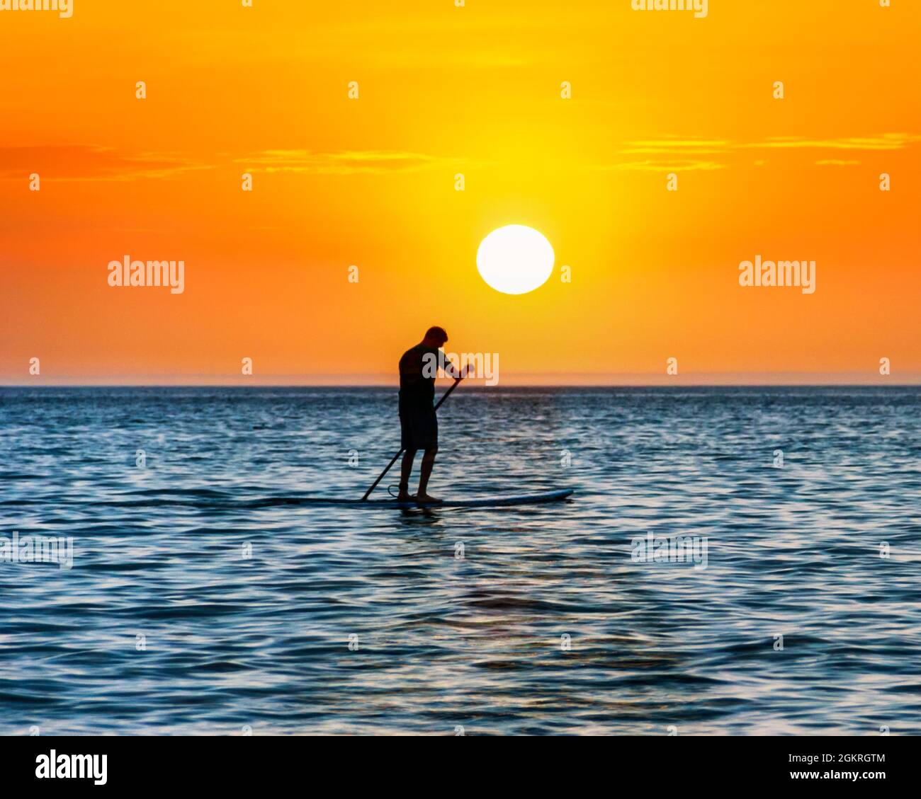 Un uomo si affaccia sul mare su una tavola da paddleboard in piedi, costeggiato dal sole che tramonta, Westward ho!, Devon, Regno Unito Foto Stock